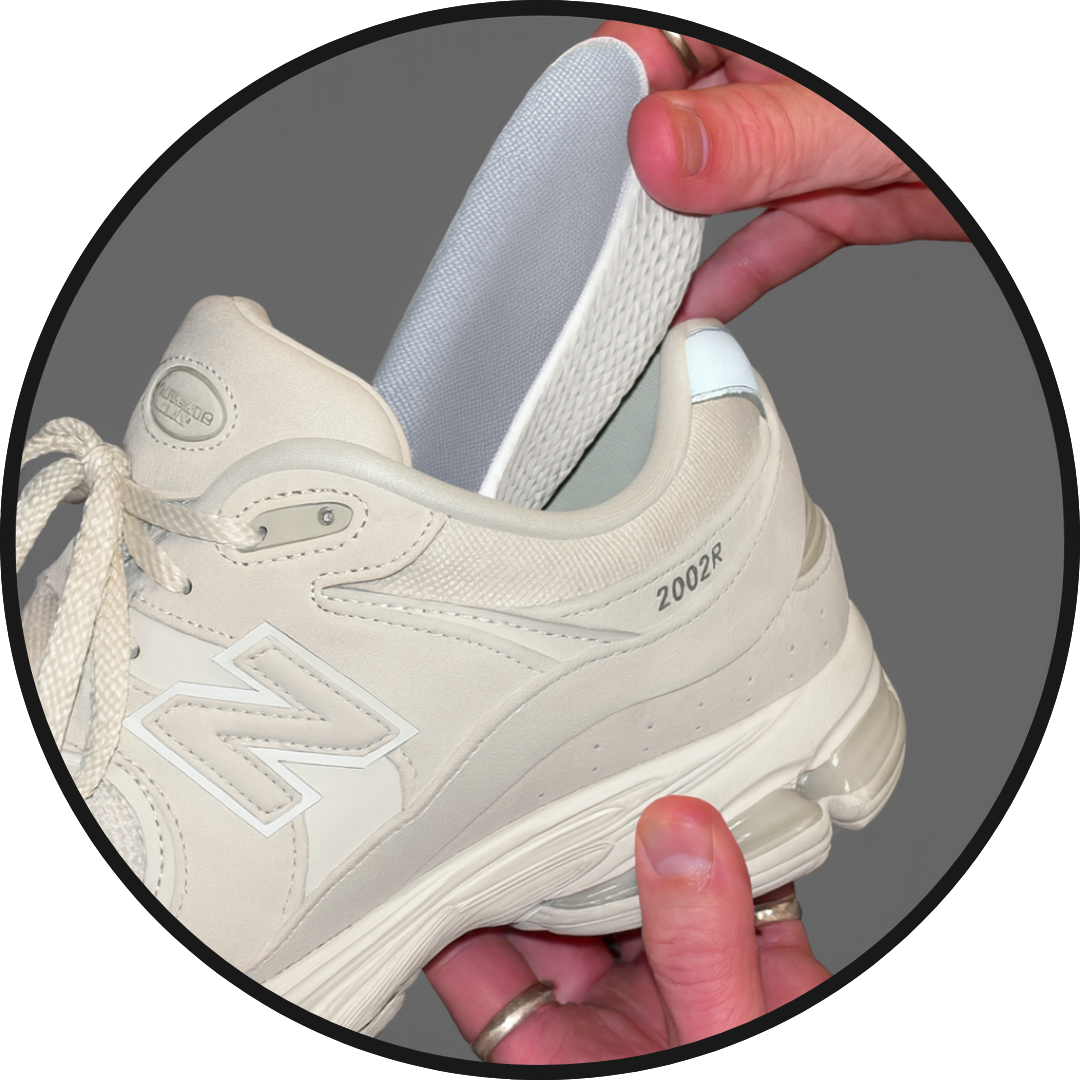 Inchmaxxers 2.0 - Height Increasing Insoles in hand being placed into new balance trainer on grey background